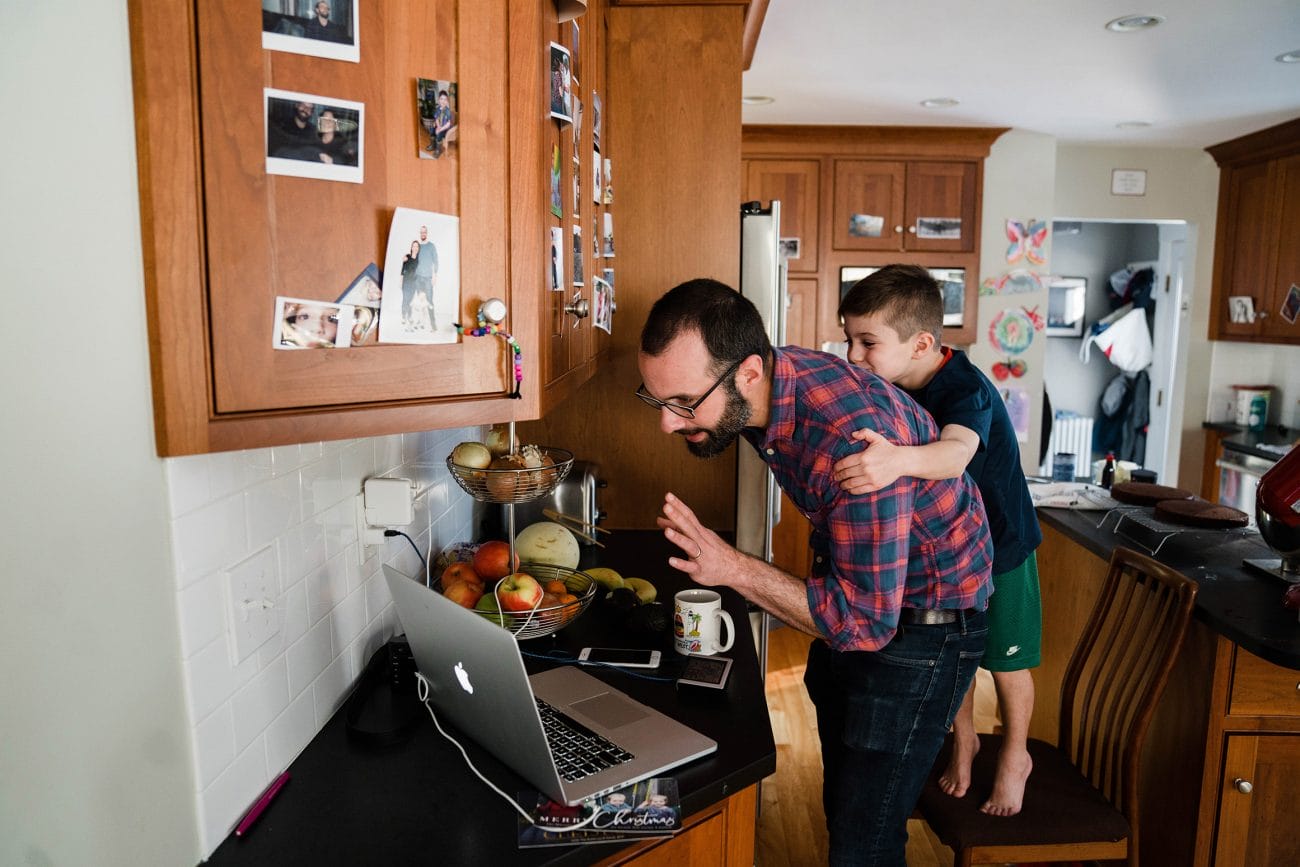 A documentary photograph of father and son waving to their family on FaceTime during an in home family session in Boston