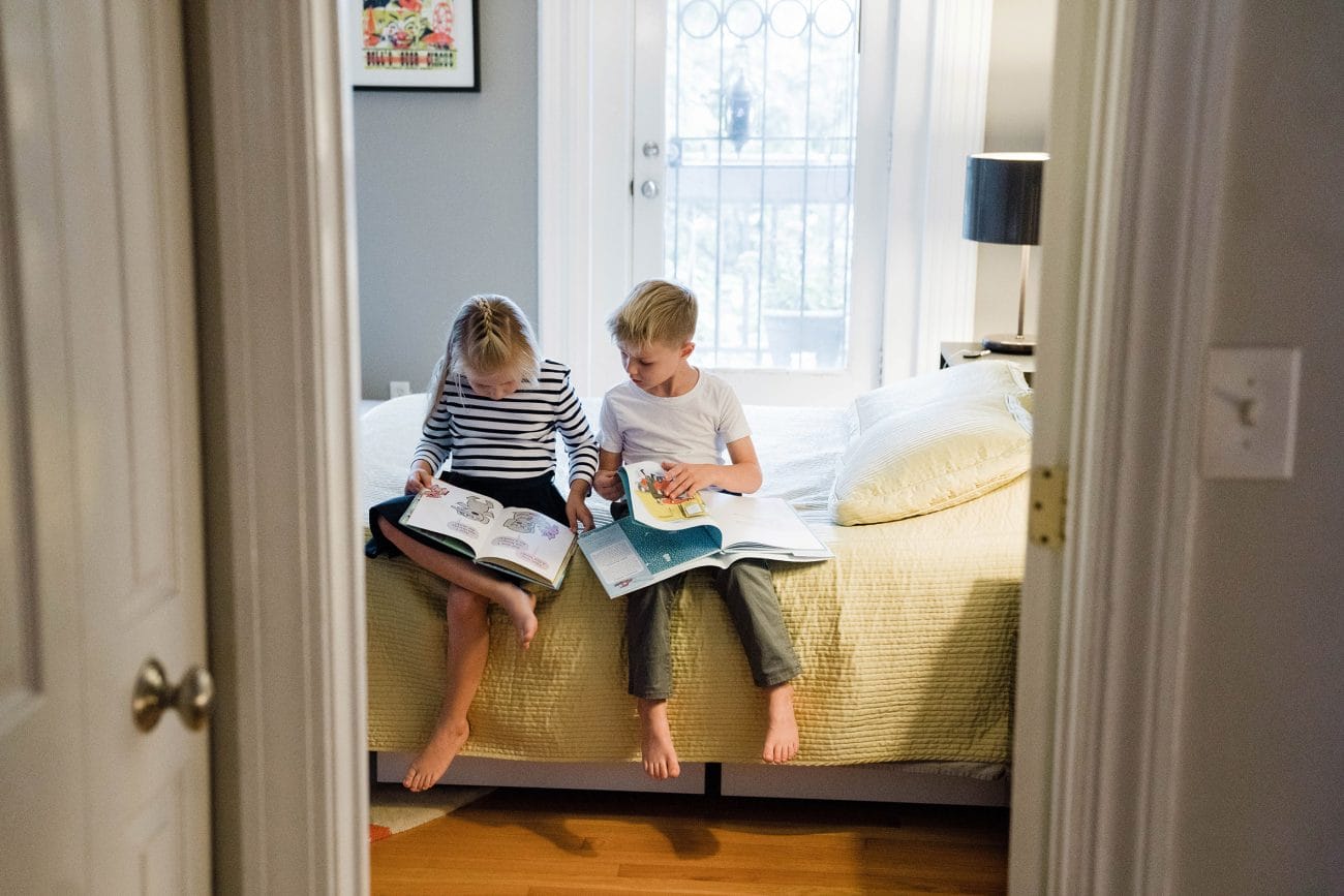 A best of Boston photograph of a brother and sister reading books in their parents bedroom during an in home family session in Boston