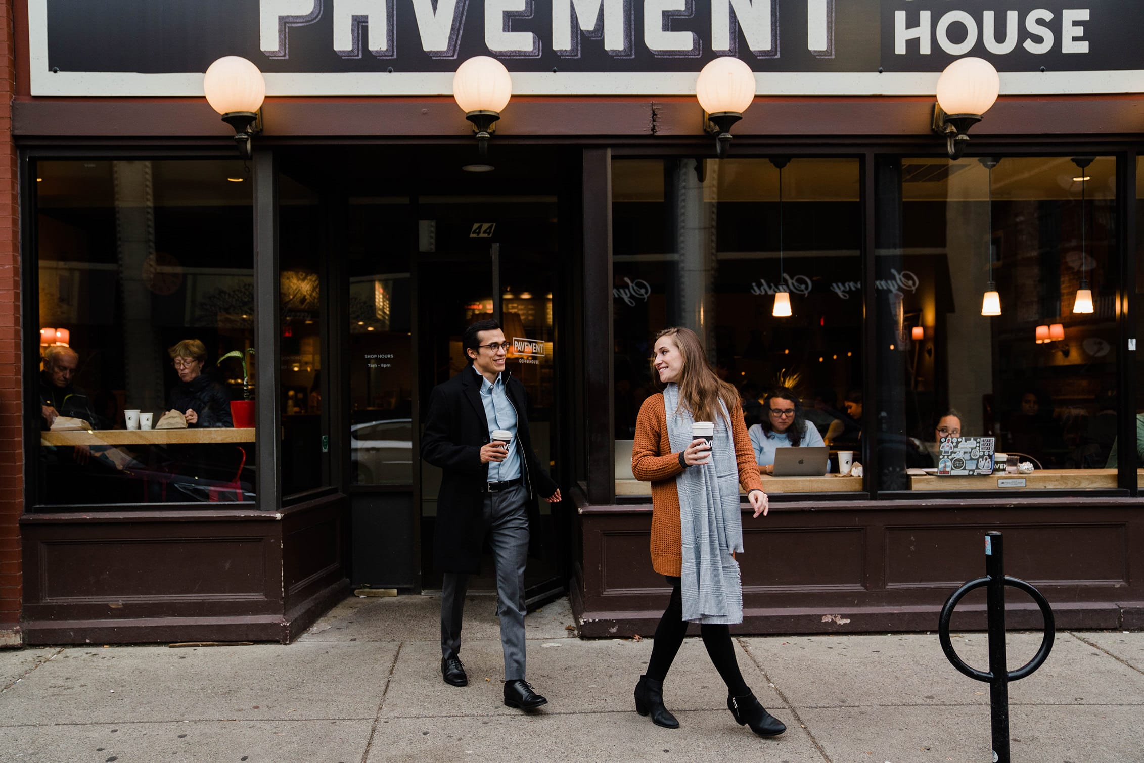 A best of Boston engagement photograph of a couple walking out of Pavement coffee house during their date night engagement session