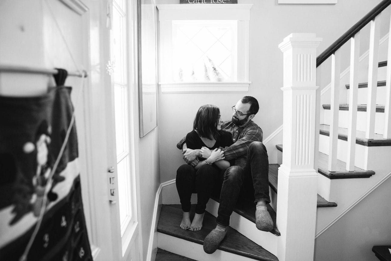 A documentary photograph of parents hugging each other on the stairs during their in home family session in Boston