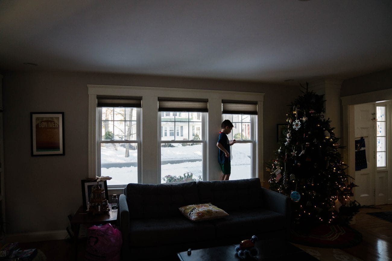 A documentary photograph of a boy playing in the window during an in home family session in Boston