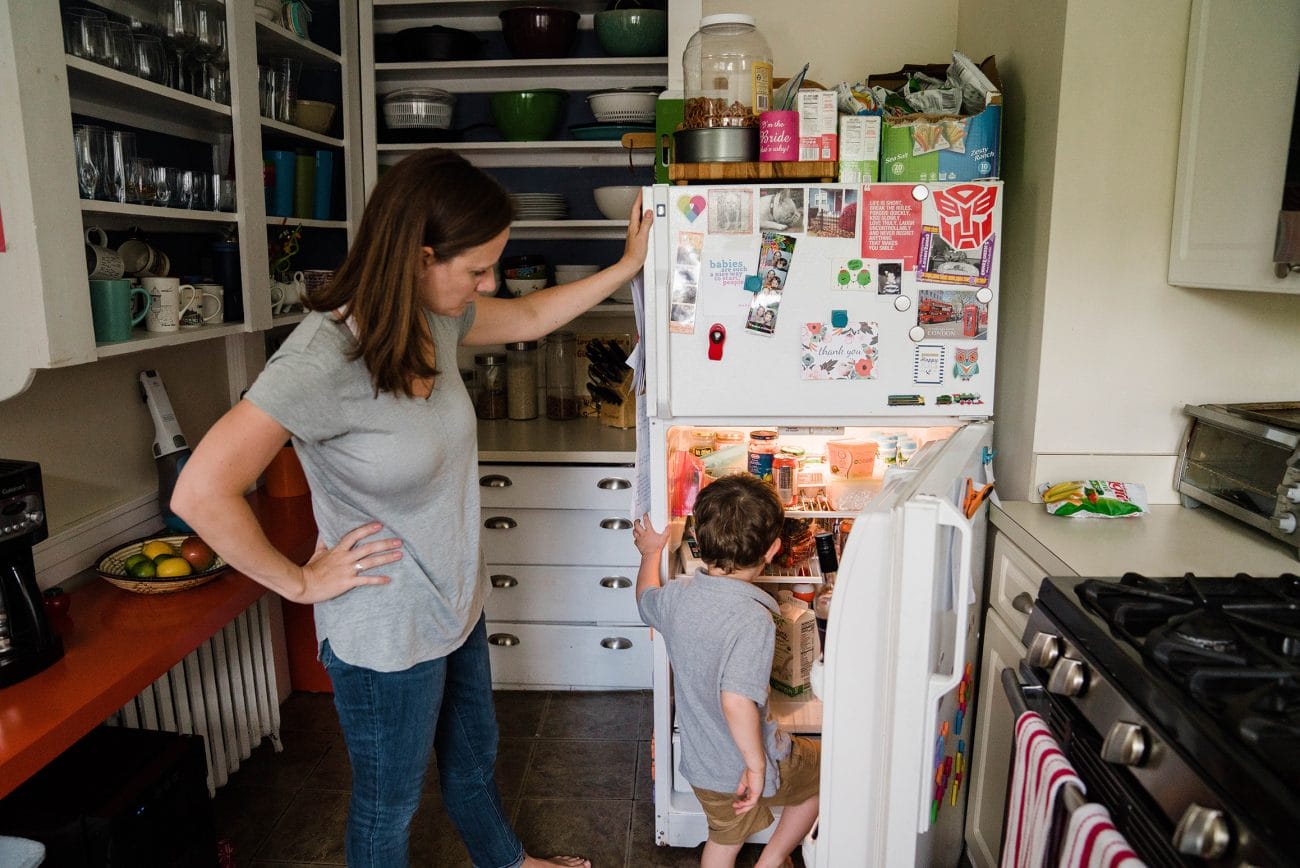 A documentary photograph of a boy finding something to eat in the fridge during an in home family session in Boston.