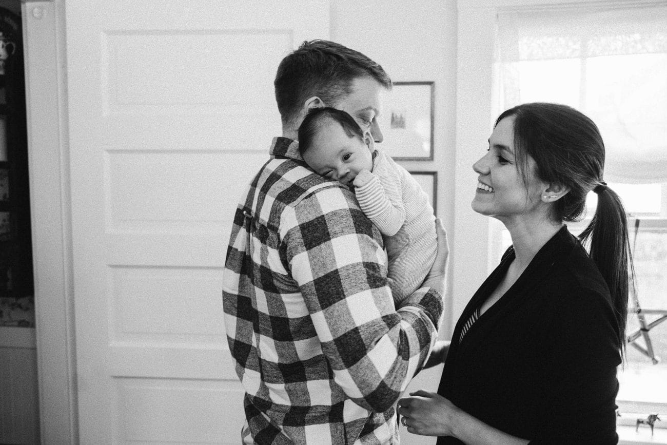 A documentary photograph of a new mom smiling at her husband and baby during an in home family session in Boston