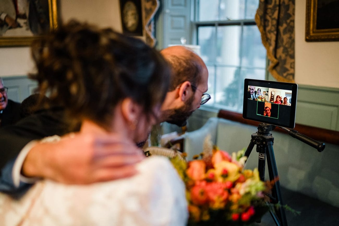 A documentary photograph of bride and groom talking to guest via zoom during their Loring Greenough House Wedding. 
