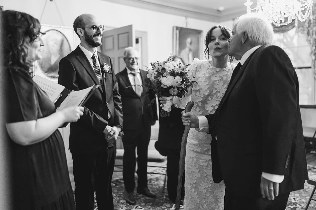 A documentary photograph of bride kissing her dad as she walks up the aisle during her Loring Greenough House Wedding. 