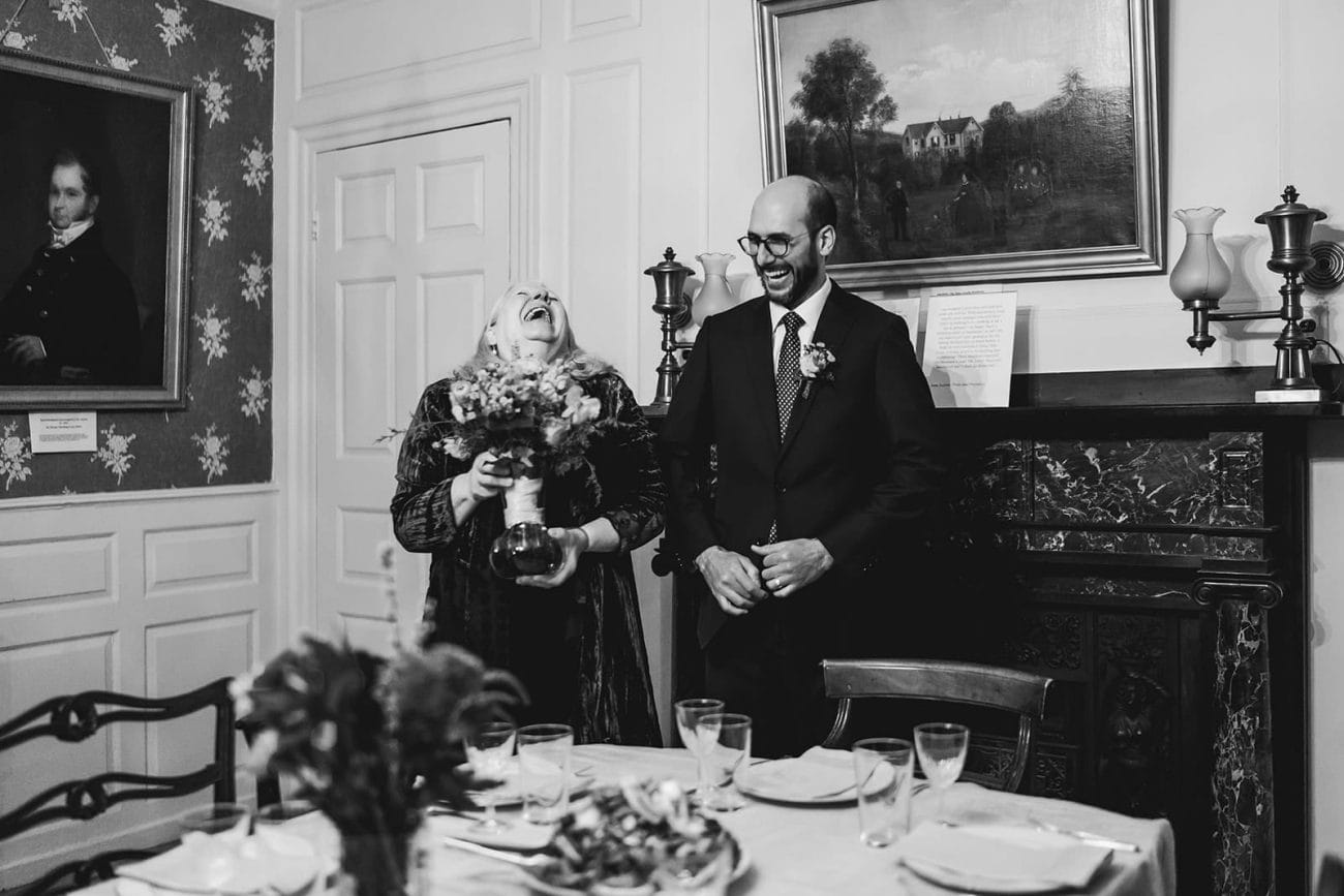 A documentary photograph of the groom talking and laughing with guests during their Loring Greenough House Wedding.  