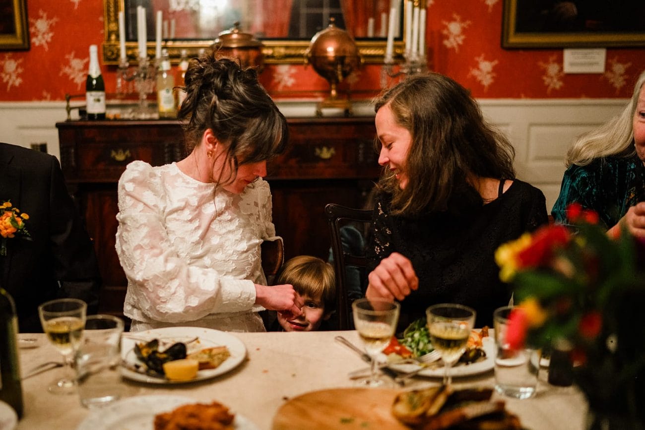 A documentary photograph of a bride and her sister laughing with their nephew during the dinner portion of their Loring Greenough House Wedding.  