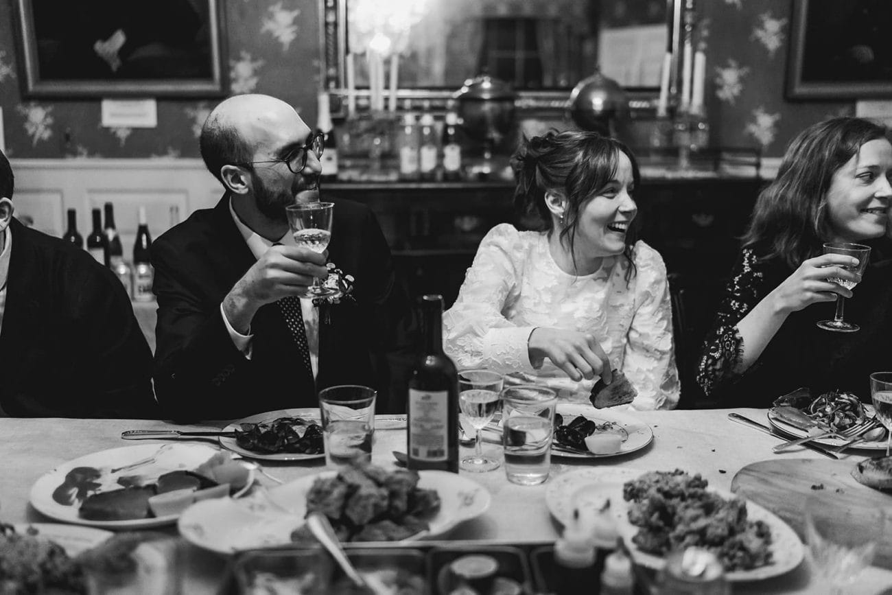 A documentary photograph of a bride and groom talking and laughing with guests during the dinner portion of their Loring Greenough House Wedding.  
