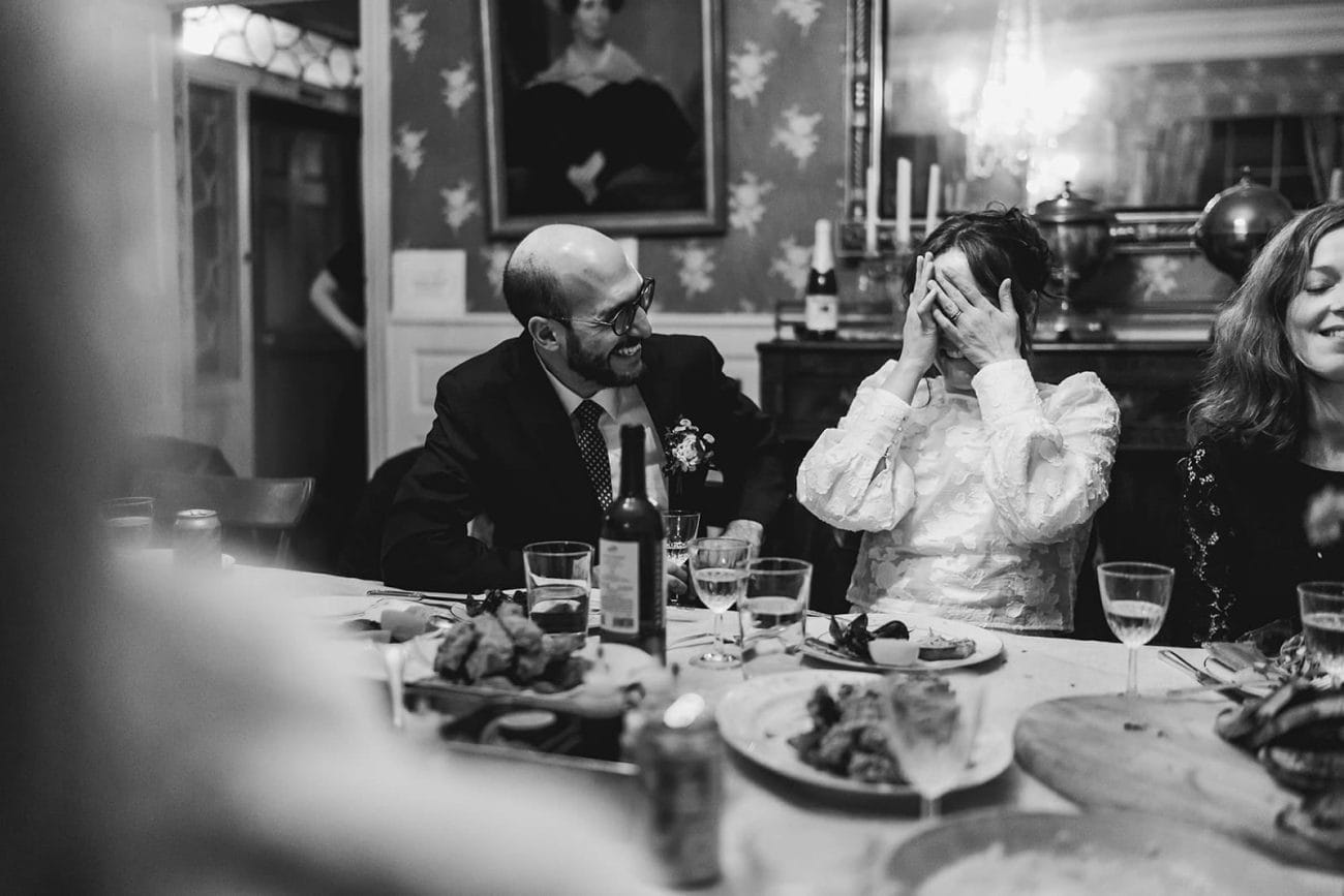 A documentary photograph of a bride and groom talking and laughing with guests during the dinner portion of their Loring Greenough House Wedding.  