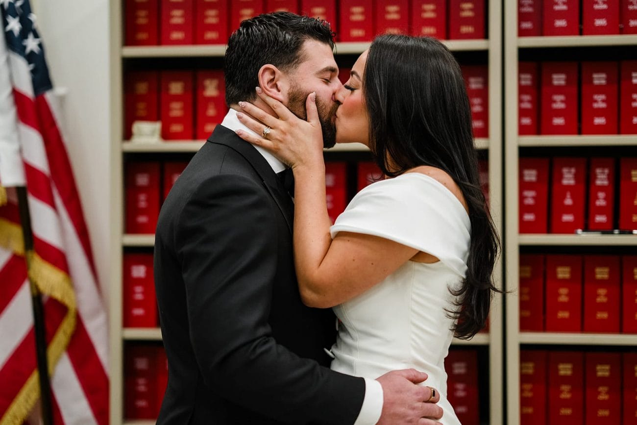 A documentary photograph of a bride and groom kissing during their ceremony at Boston City Hall before their wedding celebration at Mooo.... Seaport.