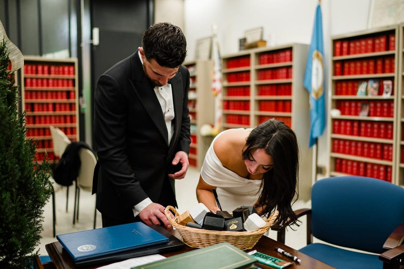 A documentary photograph of a bride and groom signing their marriage license at Boston City Hall before their wedding celebration at Mooo.... Seaport.
