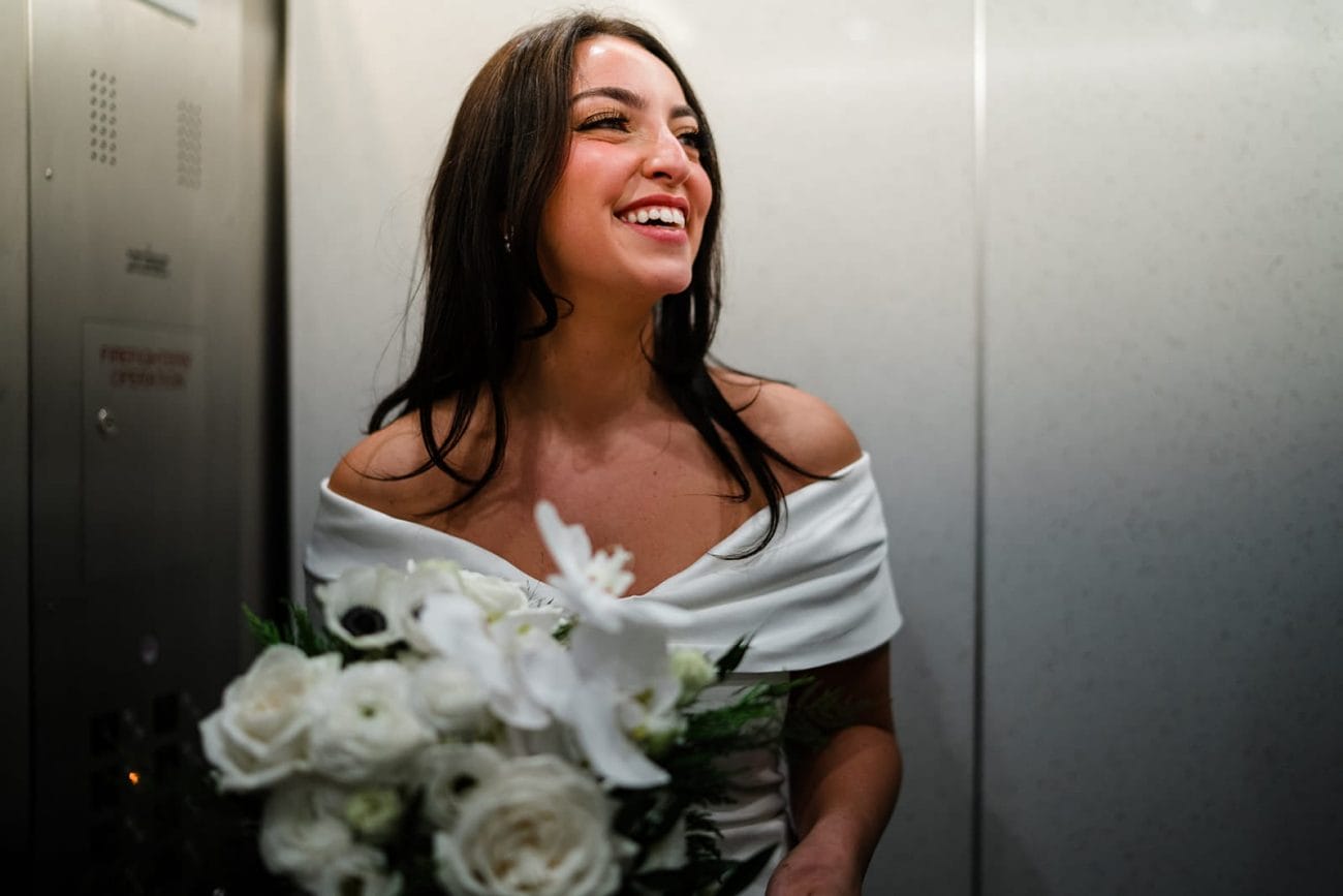 A documentary photograph of a bride laughing in the elevator at Boston City Hall before their wedding celebration at Mooo.... Seaport.