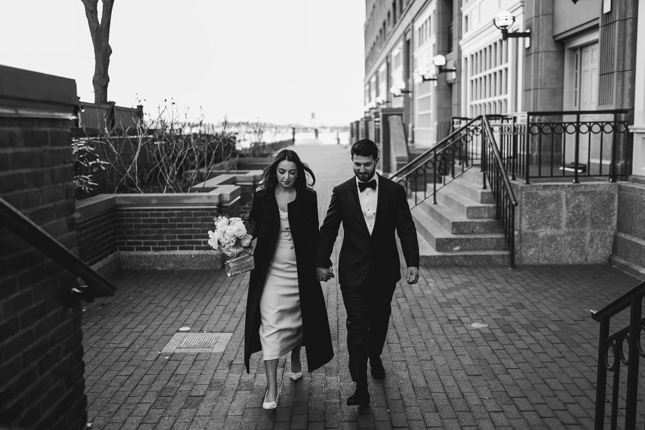A documentary photograph of a bride and groom walking through the Boston Harbor before their wedding celebration at Mooo.... Seaport.