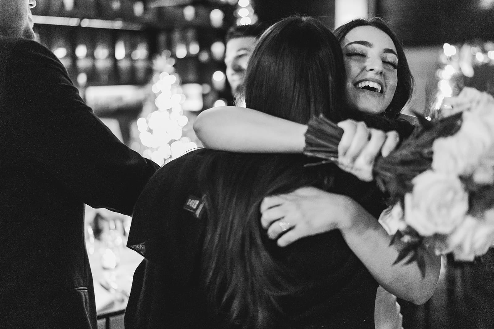 A documentary photograph of a bride hugging her friend during their wedding celebration at Mooo.... Seaport.