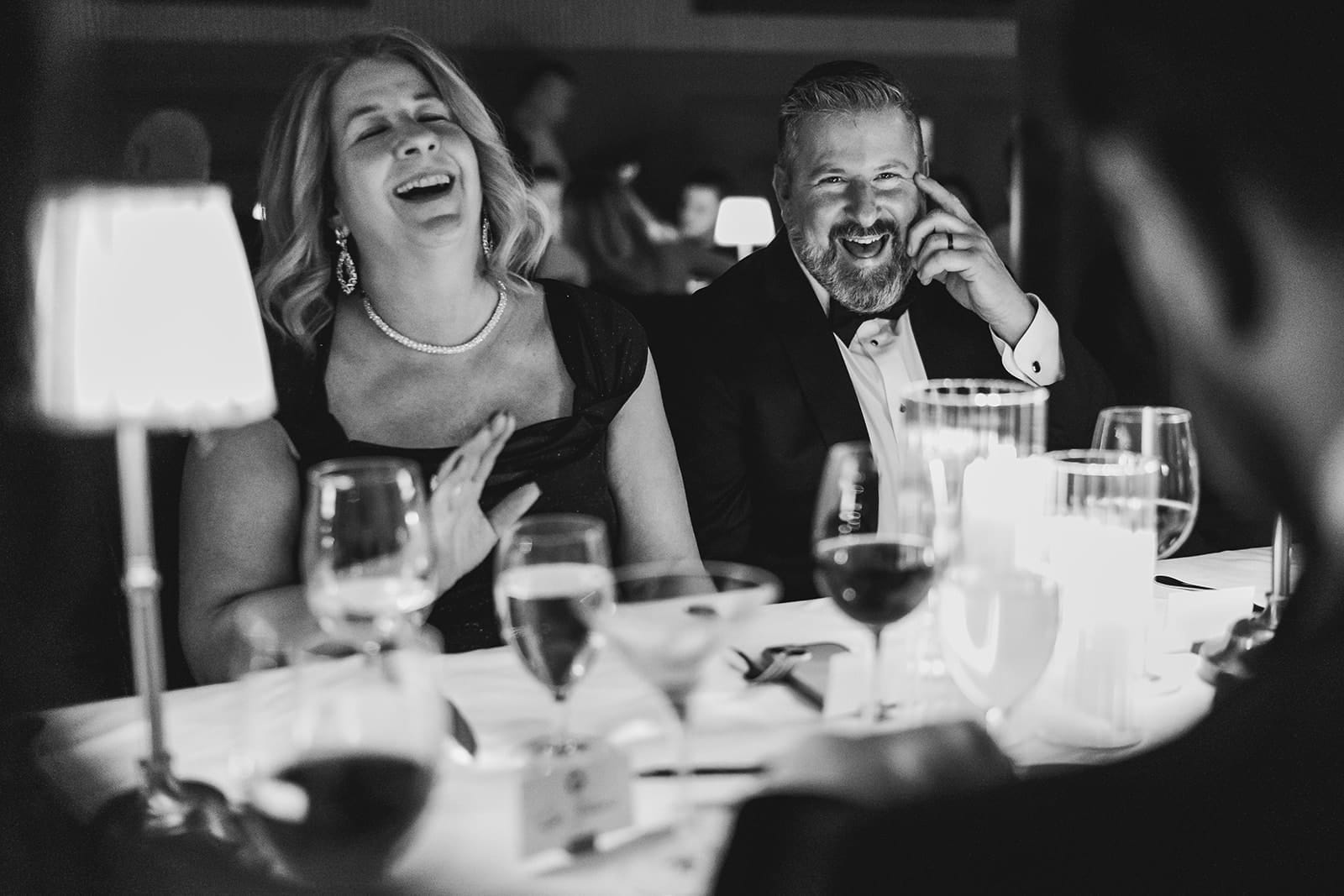 A documentary photograph of the groom's parents laughing at dinner during a wedding celebration at Mooo.... Seaport.