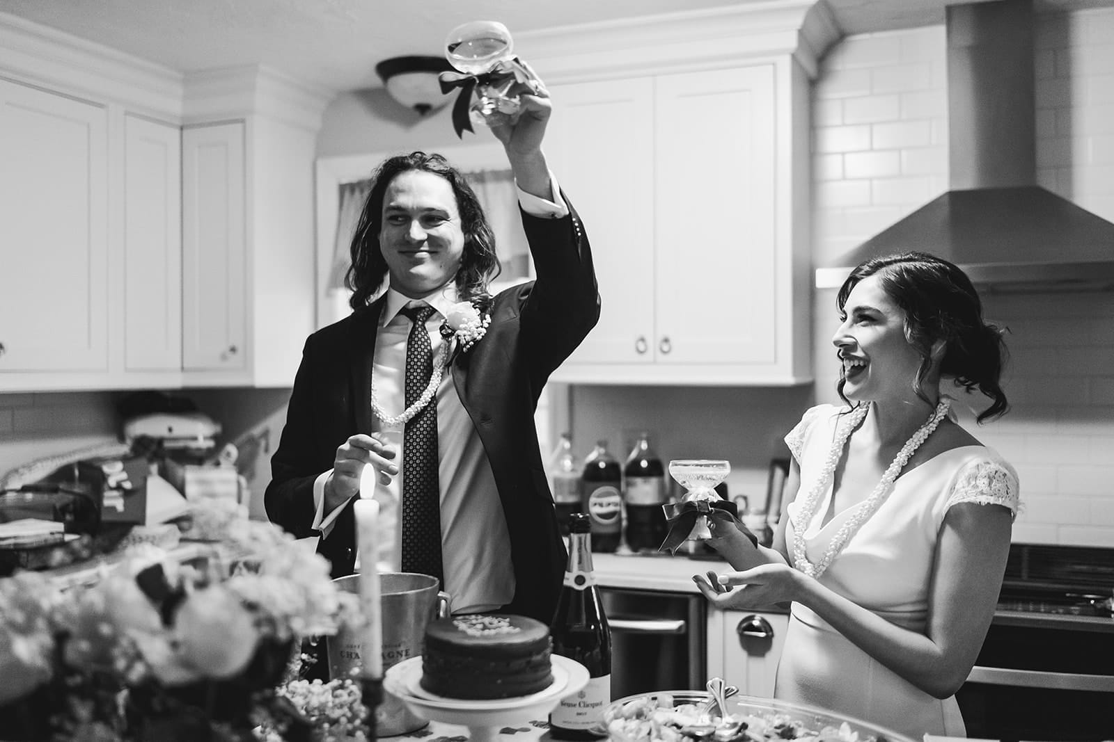 A documentary photograph of a bride and groom laughing in the kitchen during a in home celebration after their intimate Worcester Art Museum Wedding ceremony