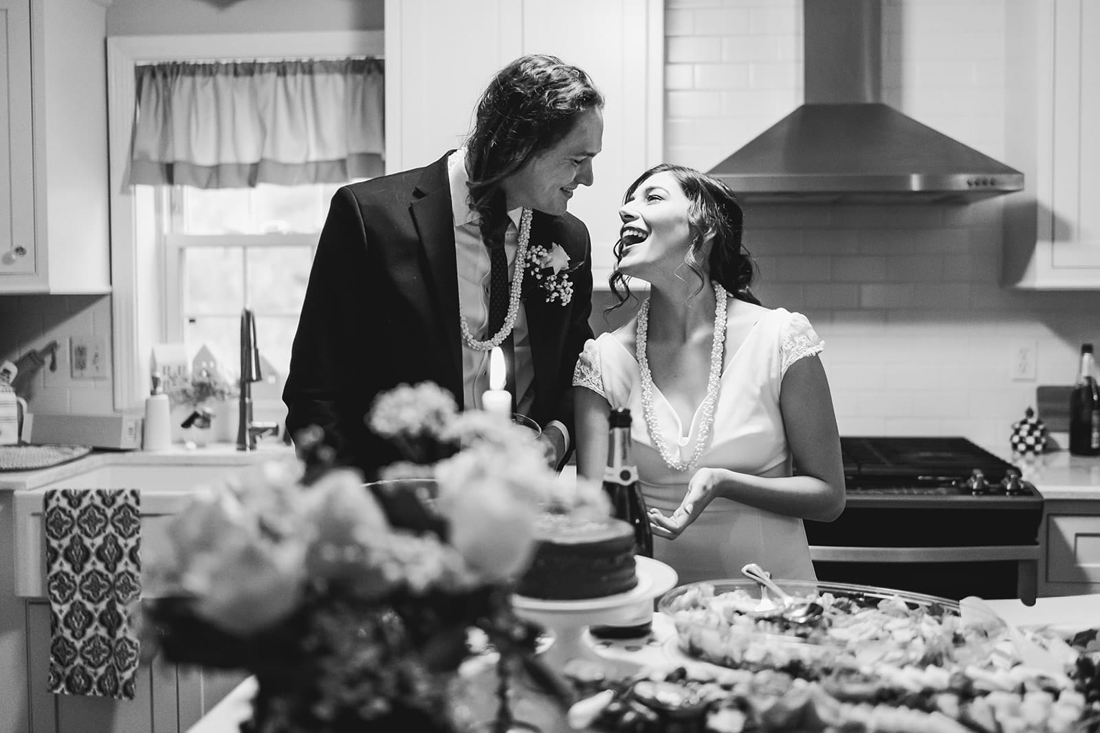 A documentary photograph of a bride and groom laughing in the kitchen during a in home celebration after their intimate Worcester Art Museum Wedding ceremony