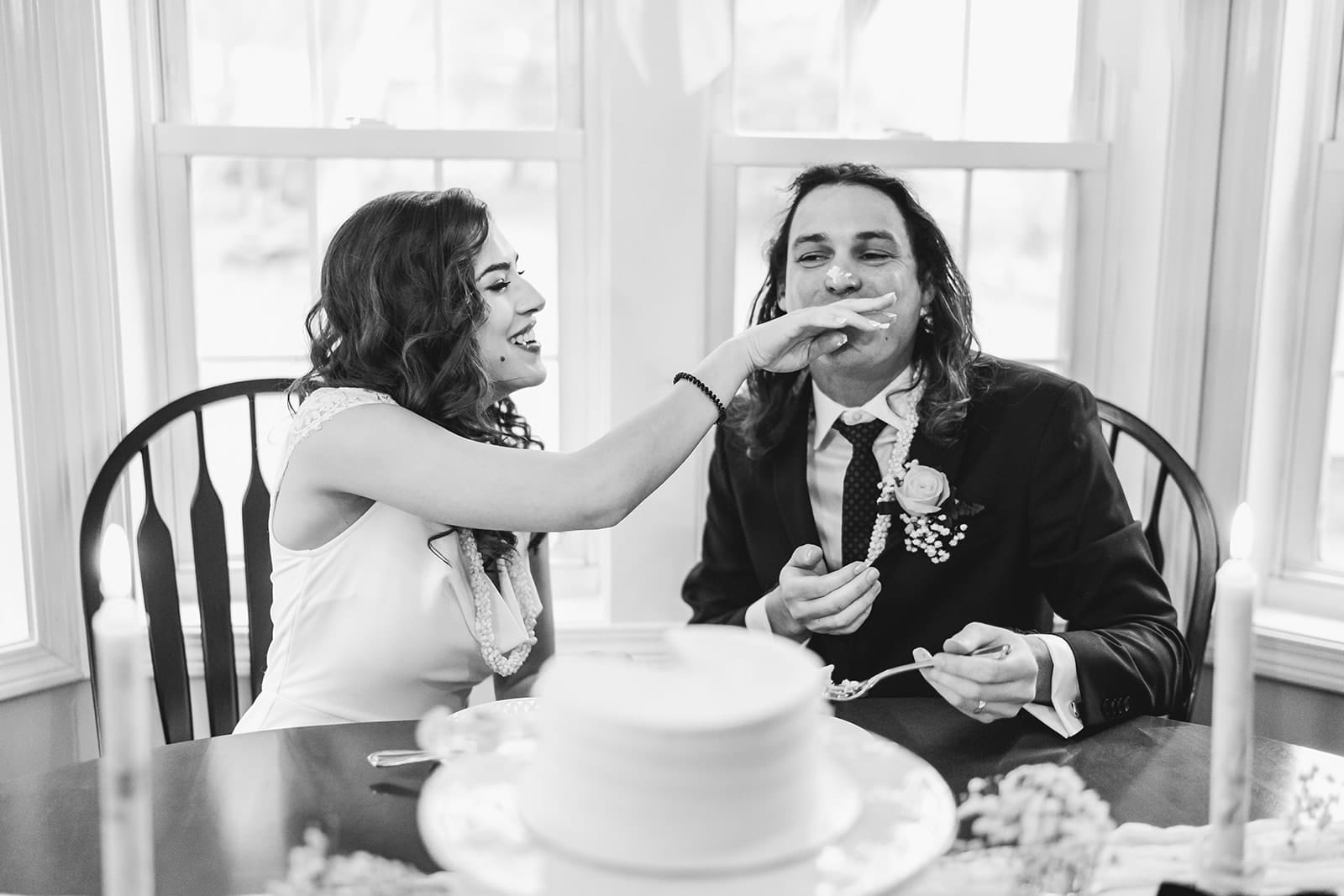 A documentary photograph of a bride and groom having cake at the kitchen table during a in home celebration after their intimate Worcester Art Museum Wedding ceremony