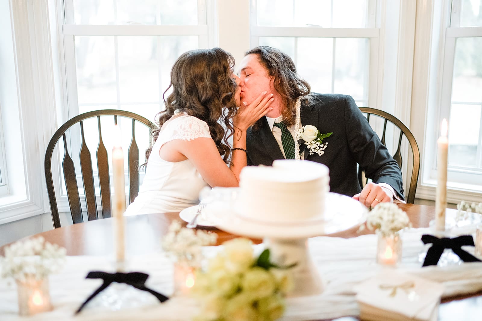 A documentary photograph of a bride and groom kissing at the kitchen table during a in home celebration after their intimate Worcester Art Museum Wedding ceremony