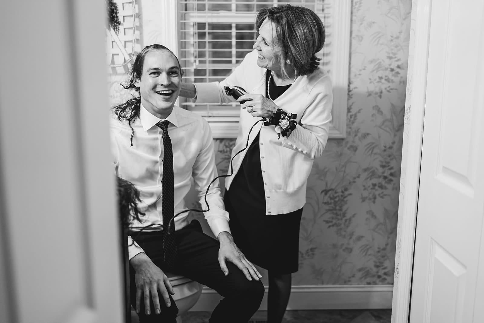 A documentary photograph of a mom shaving her son's head before cancer treatment during a in home celebration after their intimate Worcester Art Museum Wedding ceremony