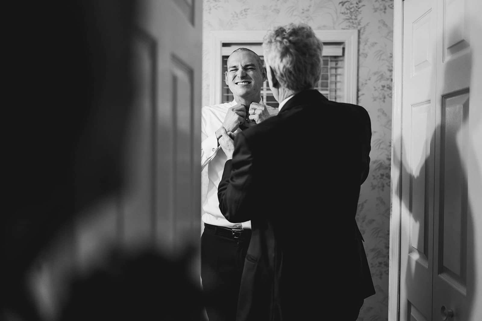 A documentary photograph of a dad helping his son with his tie during a in home celebration after their intimate Worcester Art Museum Wedding ceremony