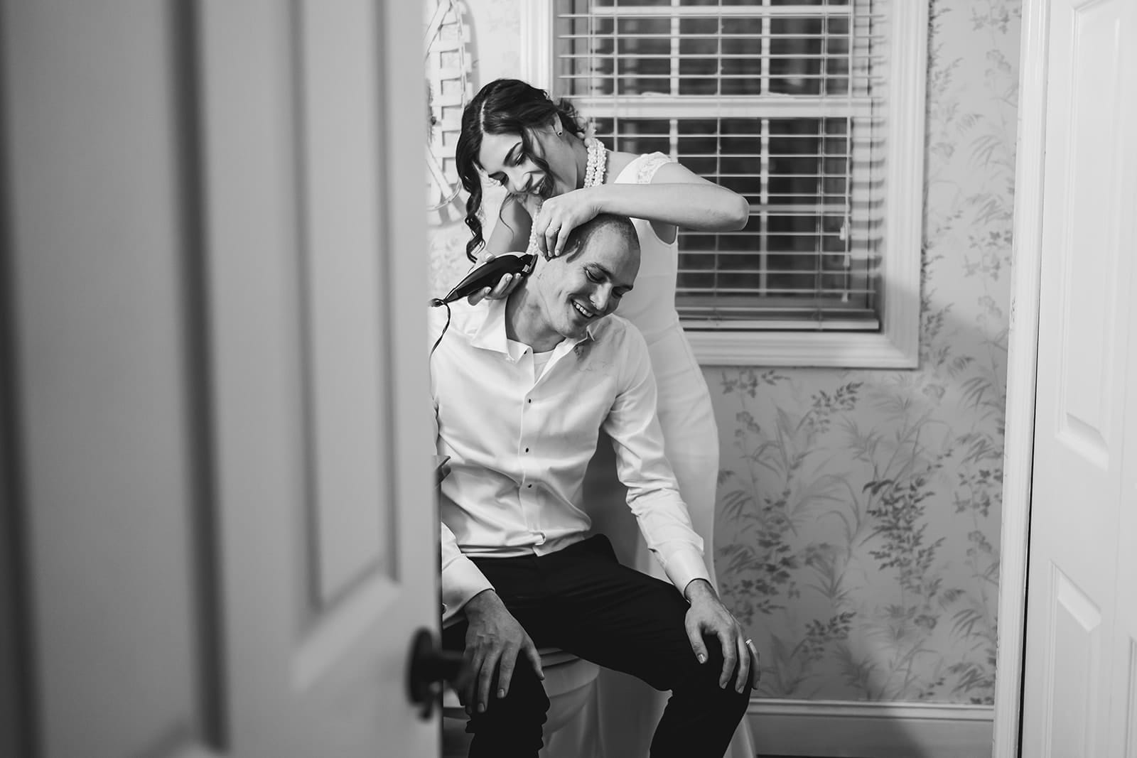A documentary photograph of a bride shaving a groom's head before cancer treatment during a in home celebration after their intimate Worcester Art Museum Wedding ceremony